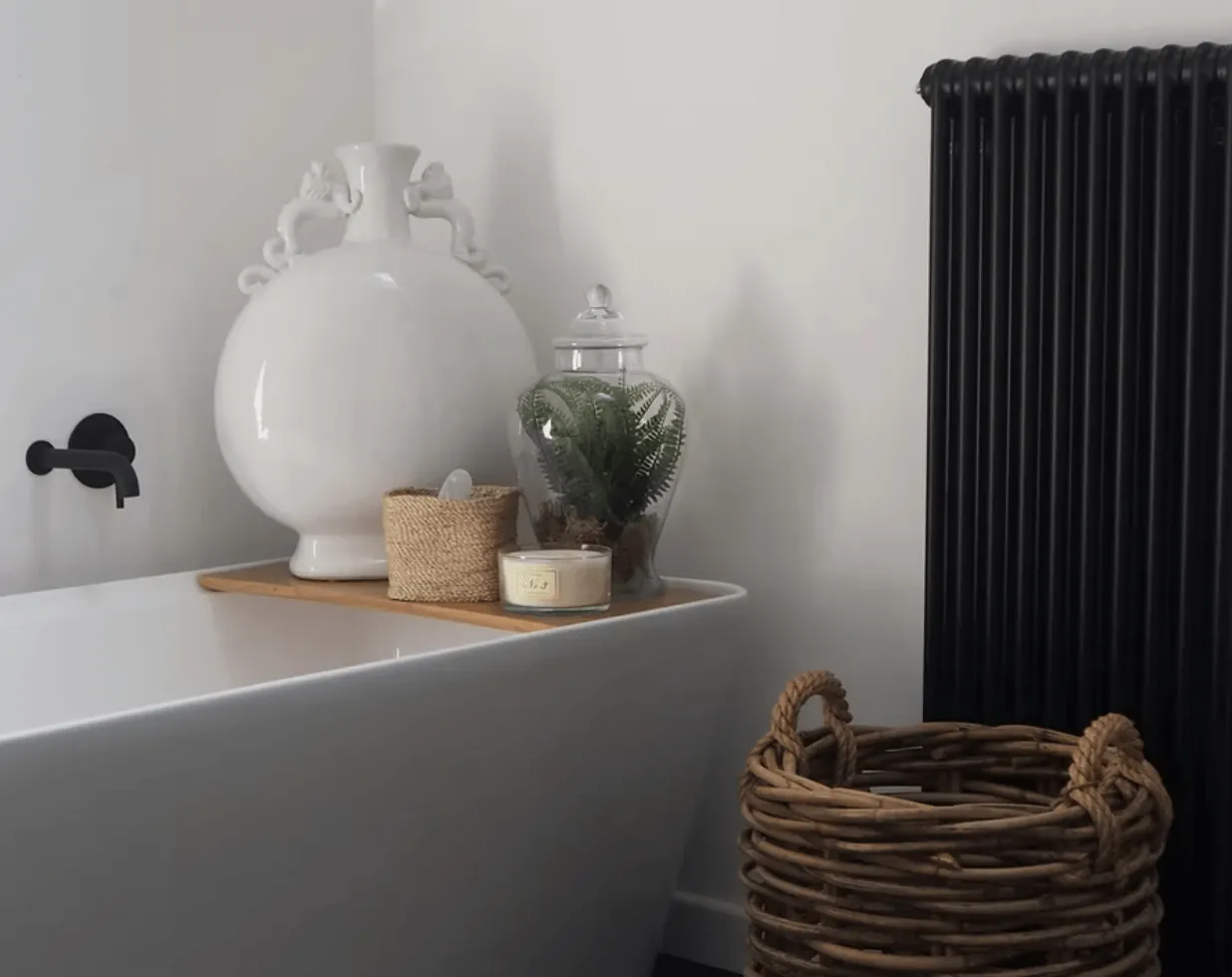 Tall black column radiator in a bathroom beside a freestanding bath