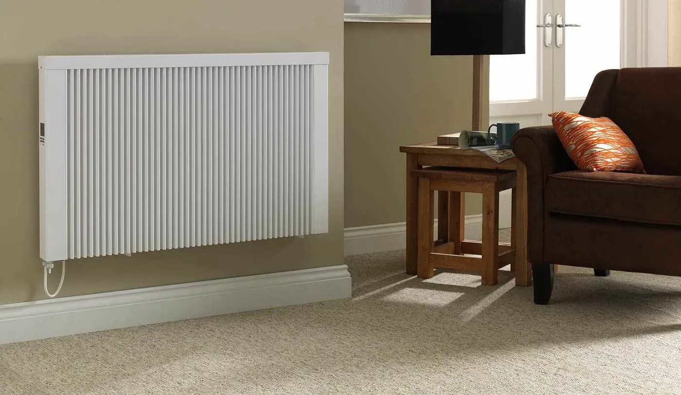 White electric radiator on a beige living room wall beside a sofa