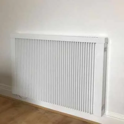 Wide white electric radiator above a wooden floor