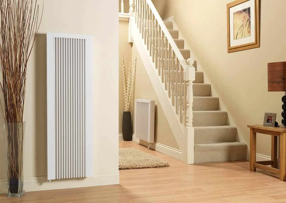 Tall vertical white radiator in a hallway beside a staircase